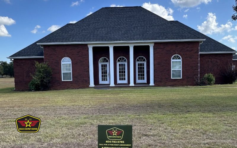 Bravo Company Roofing A single-story red brick house with white trim, four front-facing doors, and arched windows, with a realty sign in the yard and a clear blue sky above.
