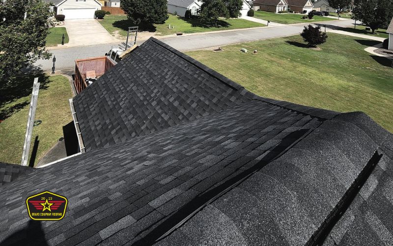 Bravo Company Roofing Aerial view of a residential roof with new dark asphalt shingles, surrounded by green lawns and houses in a suburban neighborhood.